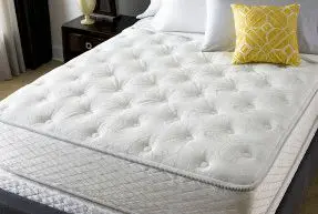 A white mattress with yellow pillows on top of it.